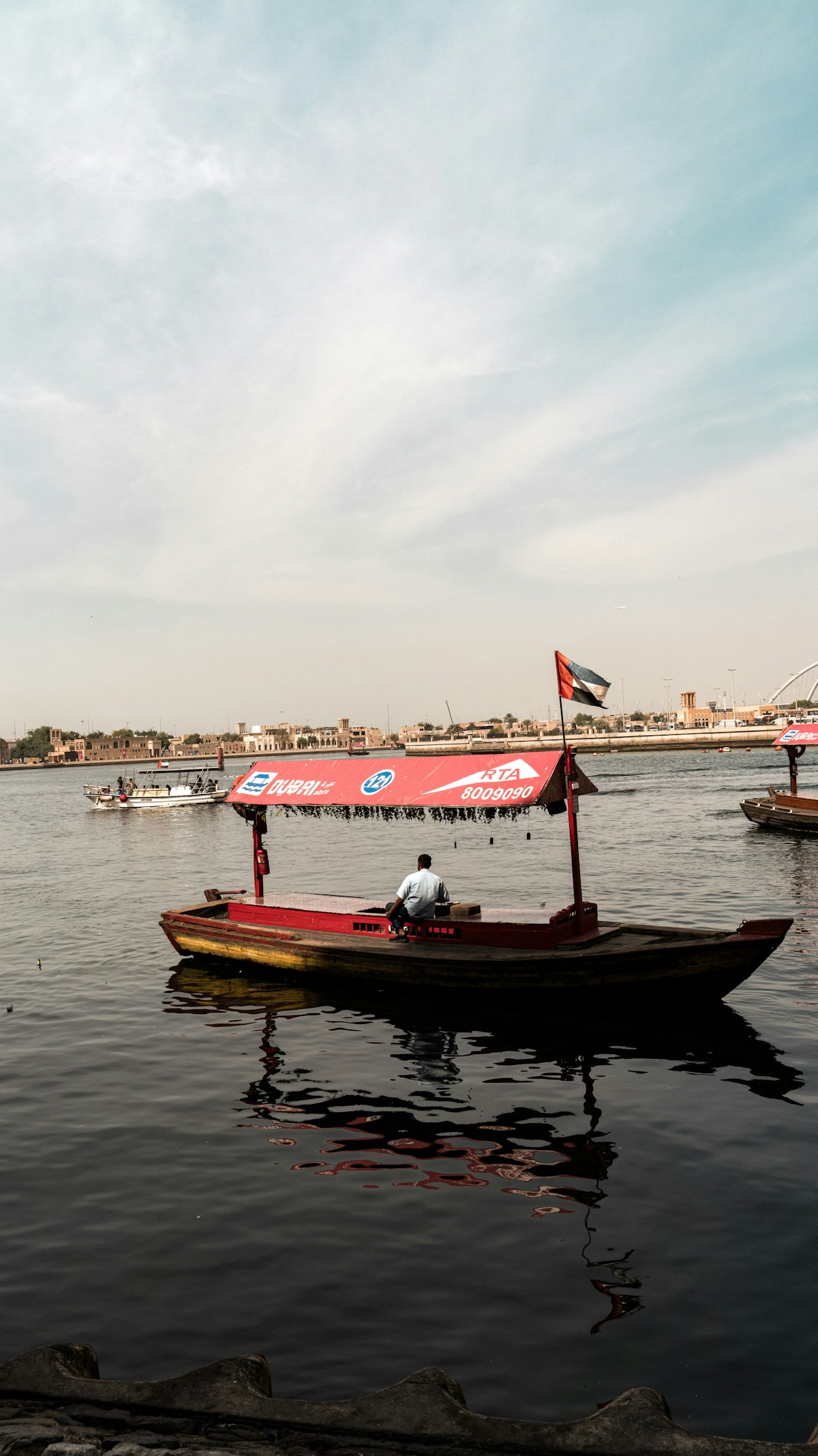 Traditional abra boat steered by a captain with UAE flag on Dubai Creek