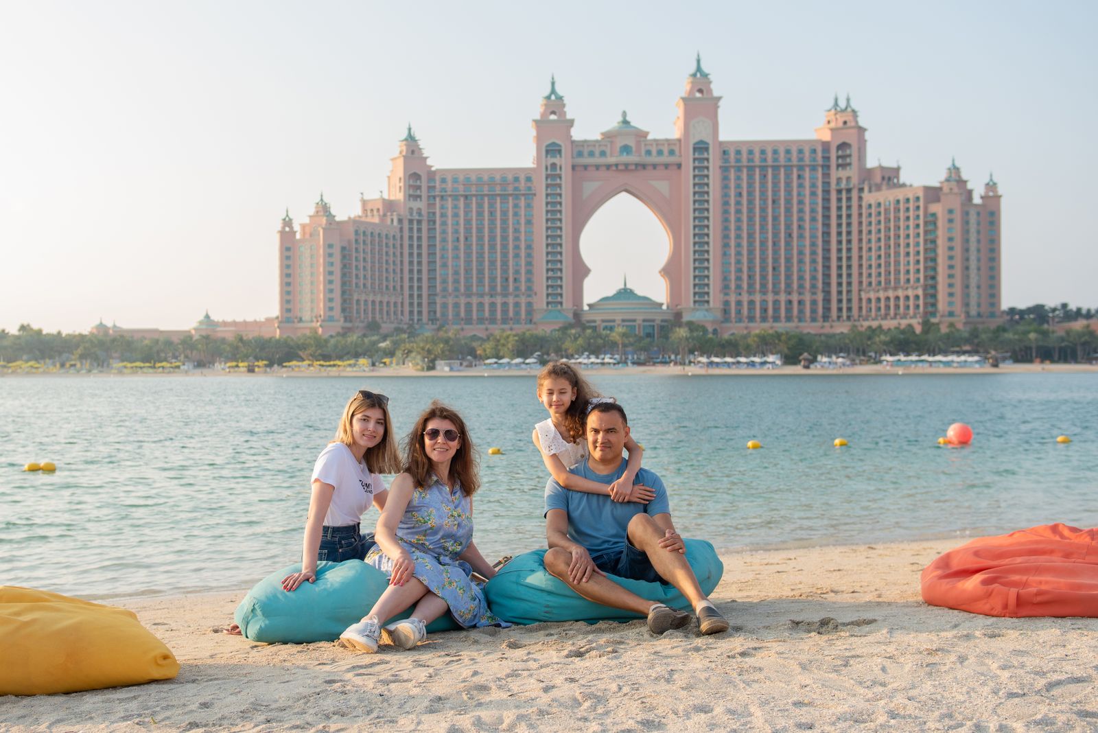 Family of four sitting on a sandy beach with the Atlantis hotel on Palm Jumeirah across the water
