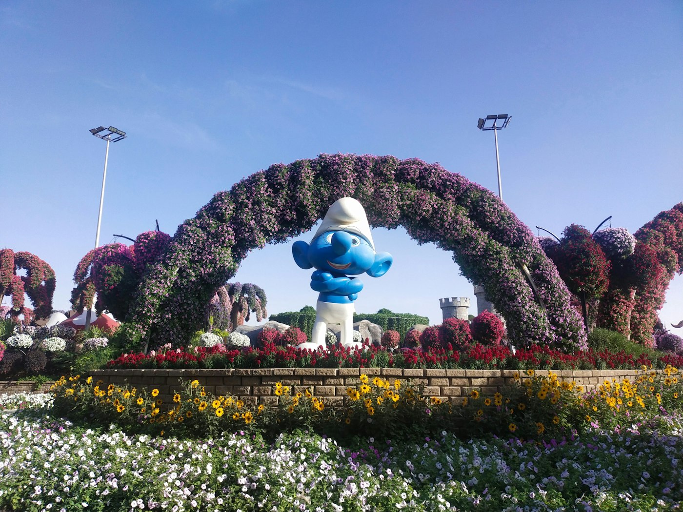 Flower arch with Smurf character at Dubai Miracle Garden with colourful blooms against a blue sky