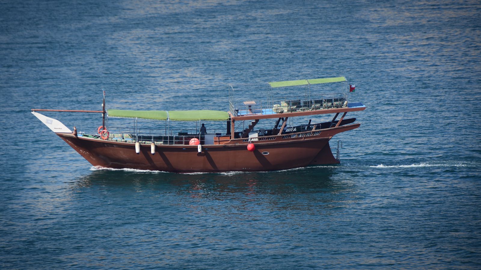 Traditional wooden dhow with an Omani flag cruising in the waters off Musandam, Oman