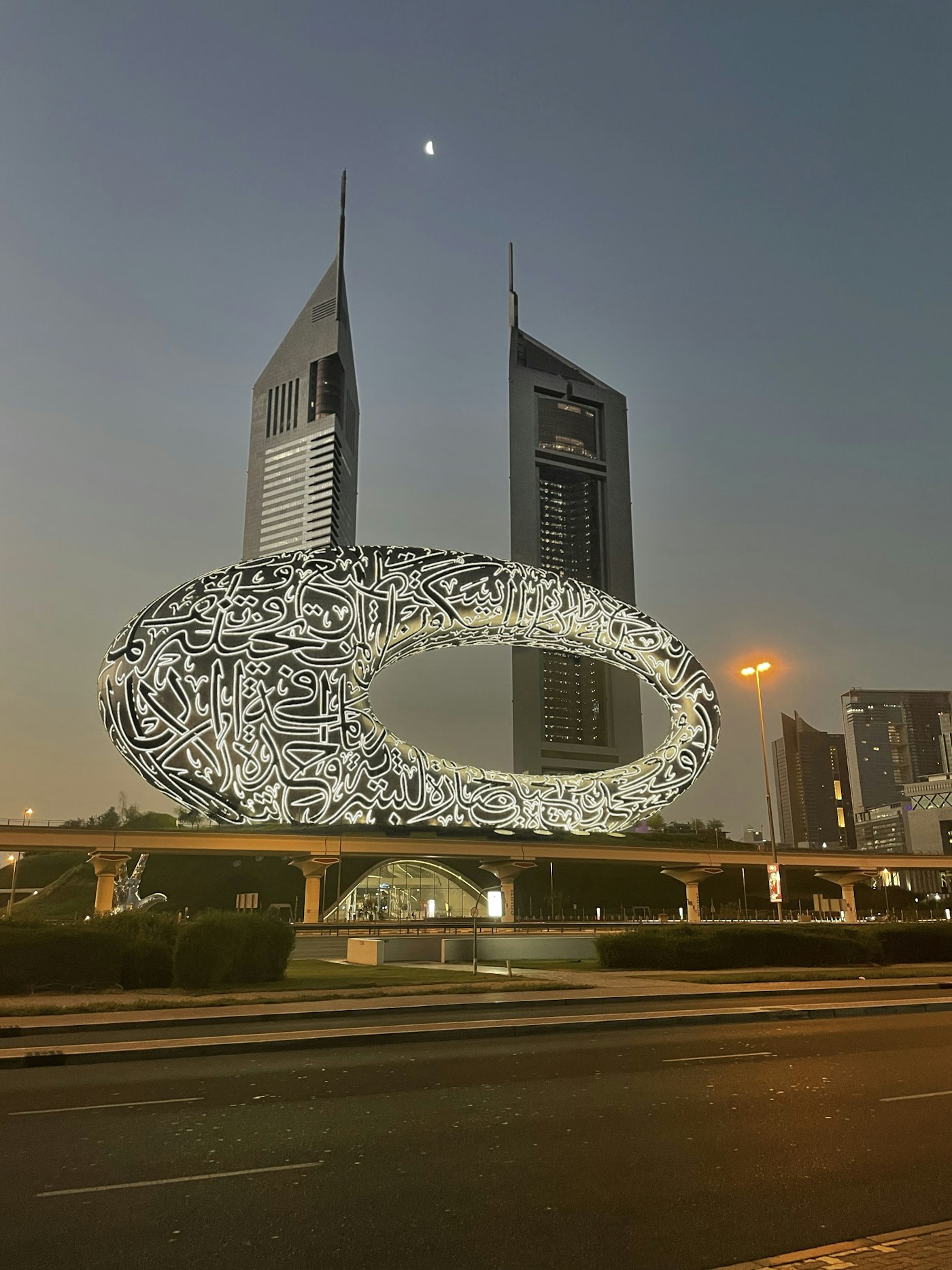 Museum of the Future Dubai at night with Arabic calligraphy on the toroid facade and Emirates Towers behind