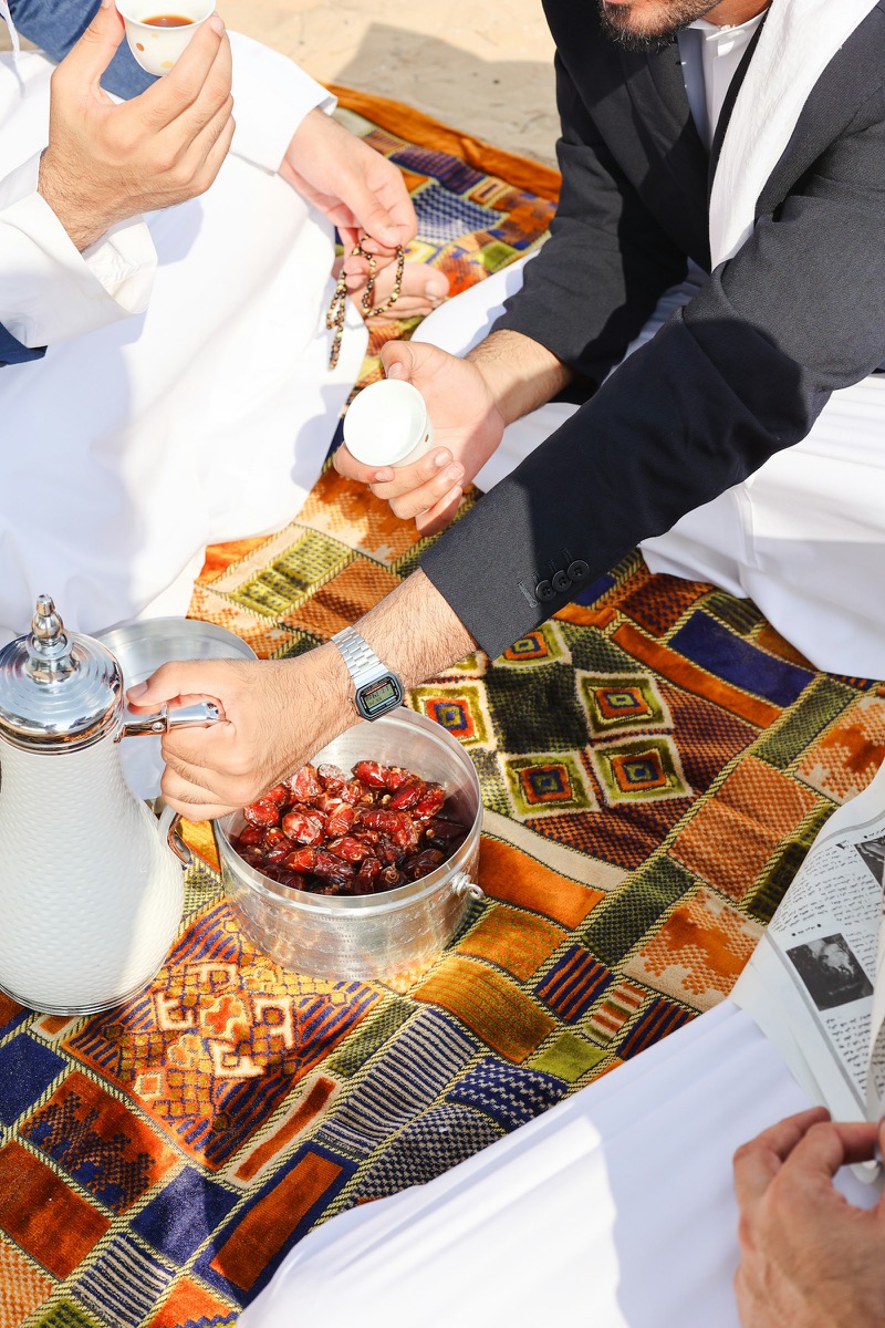 Men in traditional UAE dress sharing coffee and dates on a patterned carpet in Al Ain