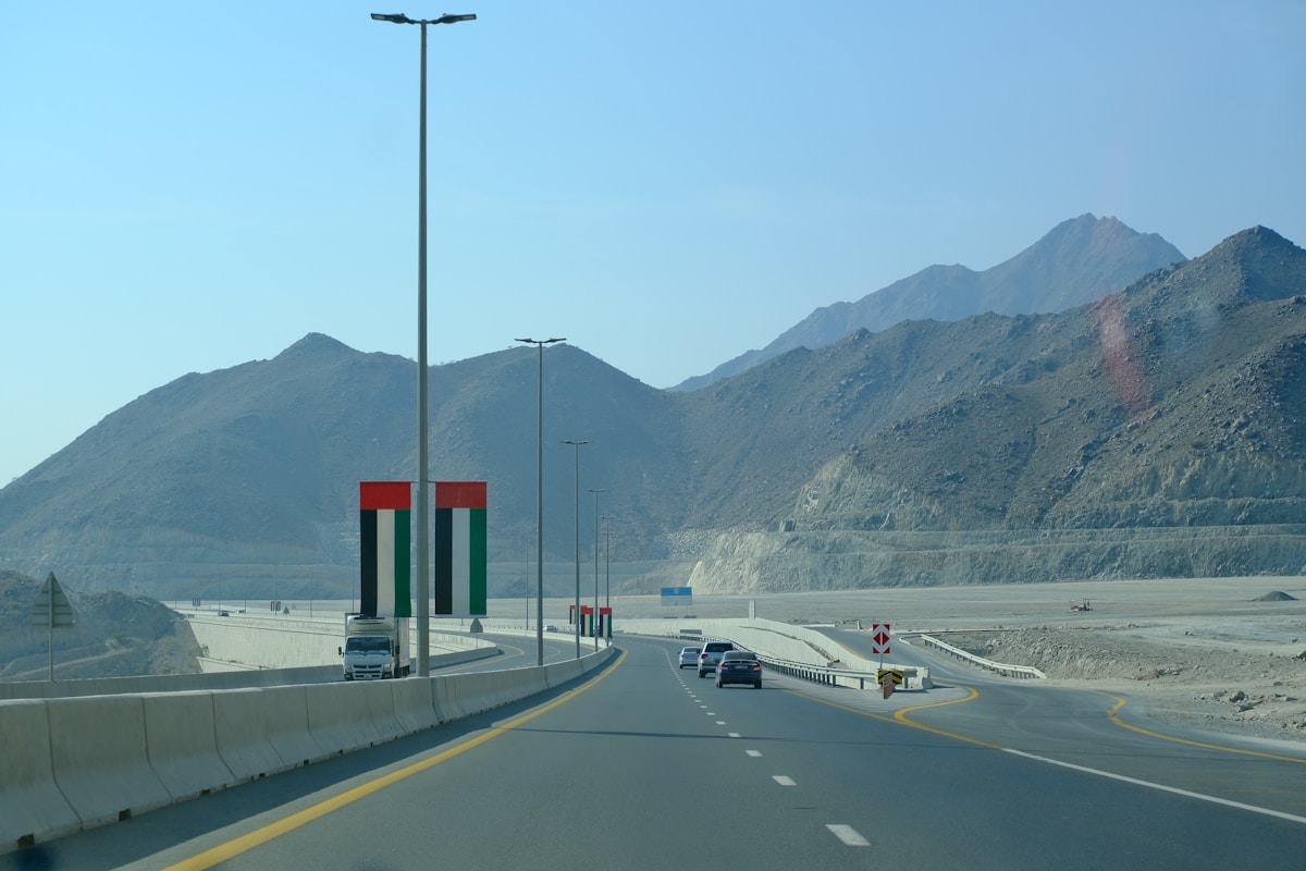 UAE highway with UAE flag pillars and mountain range in background