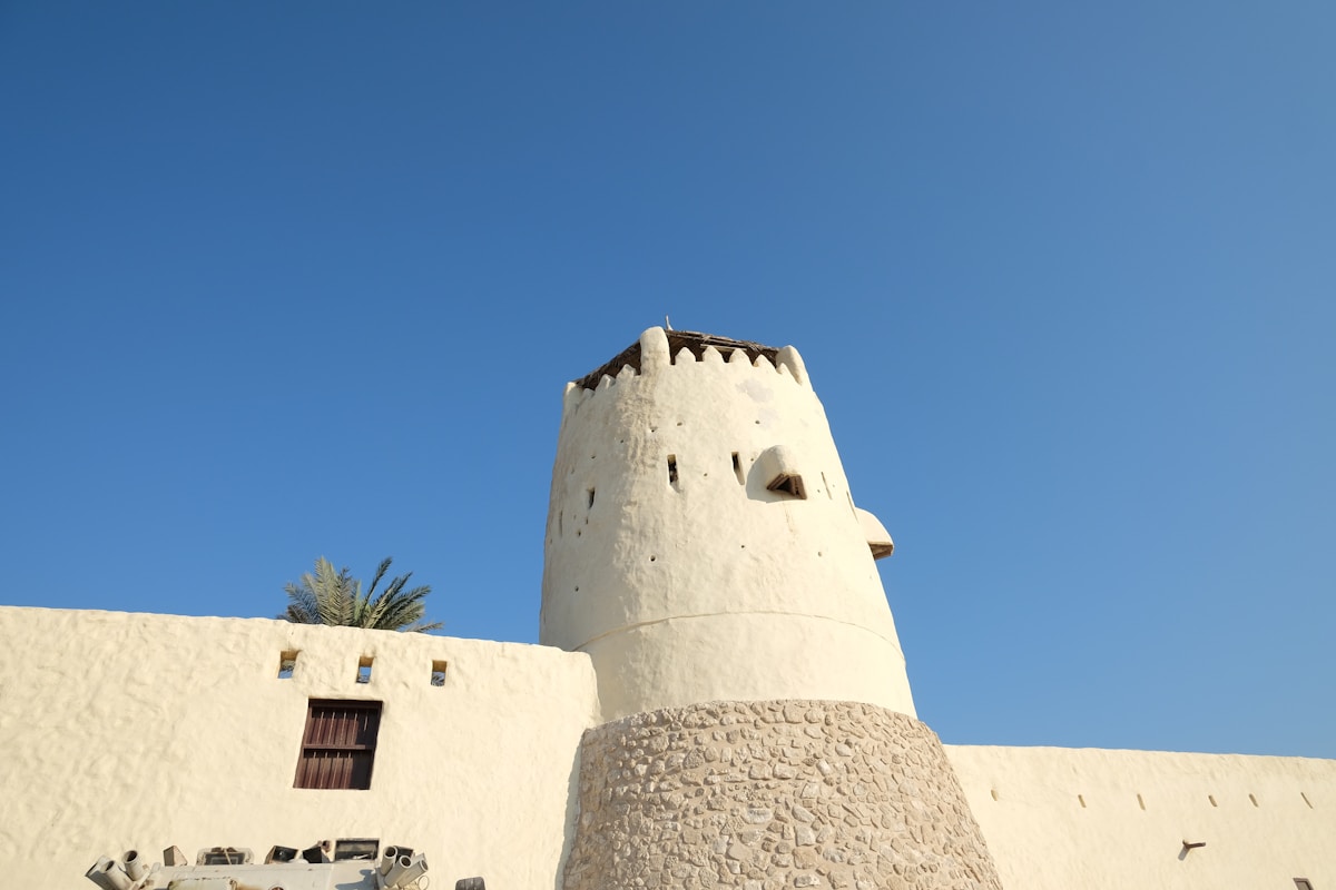 White historic fort tower against clear blue sky, Umm Al Quwain UAE