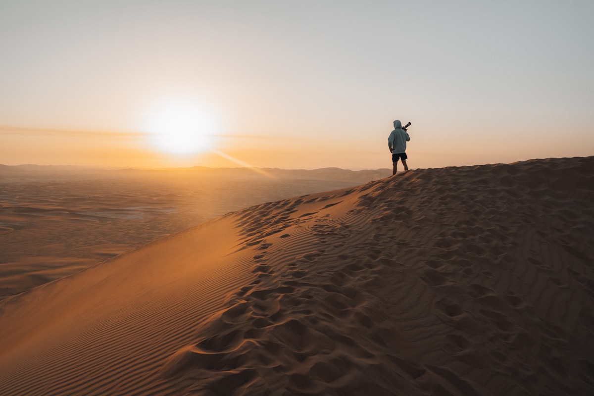 Person standing on a massive sand dune ridge at sunset in the UAE desert, Liwa