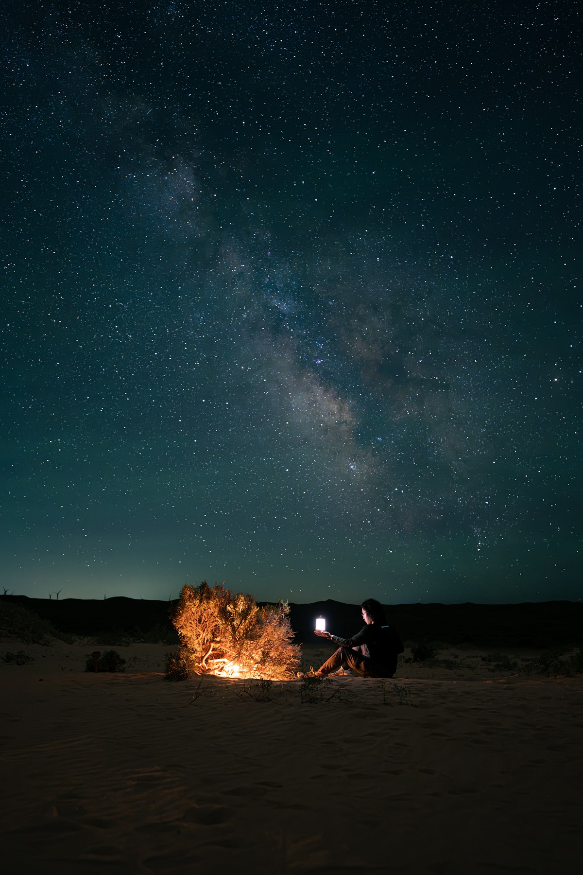 Man sitting beside a campfire under a starry night sky in the desert UAE