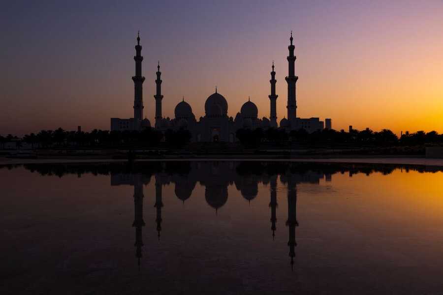 Sheikh Zayed Grand Mosque silhouetted against a sunset sky with reflection in the water