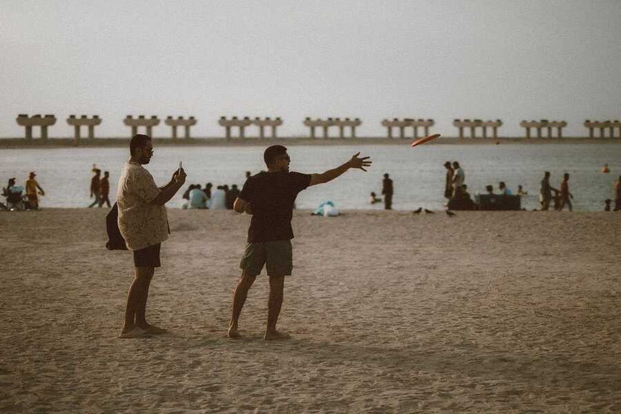 Two people tossing a frisbee on the sand at JBR Beach, Dubai