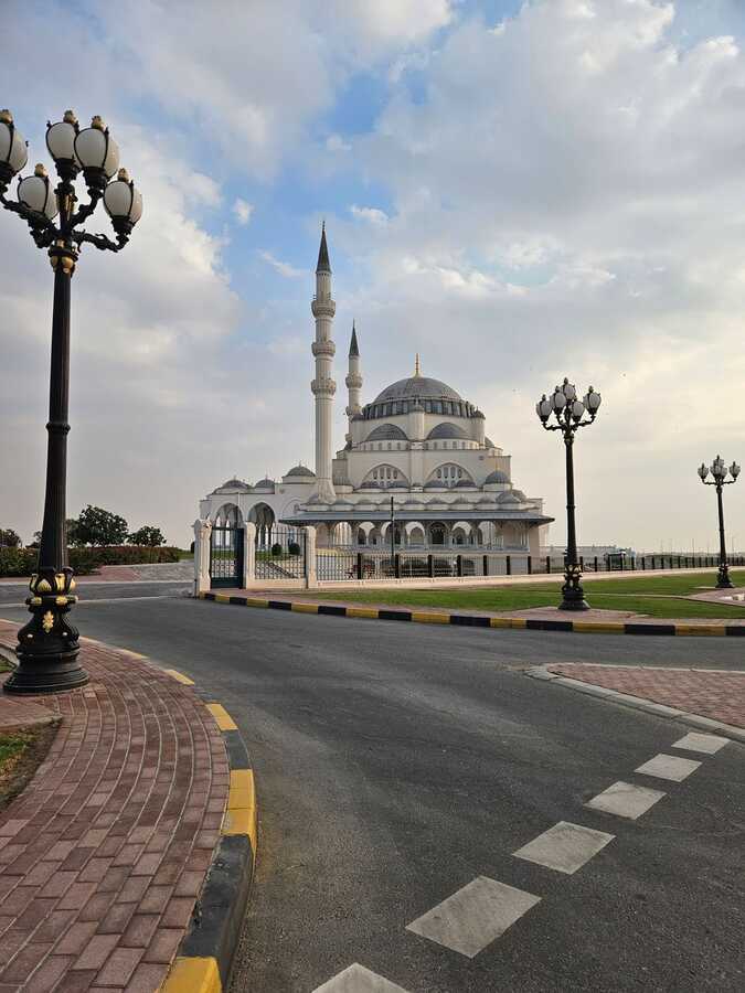 Domed mosque with minarets beside a lamp-lined road in Sharjah