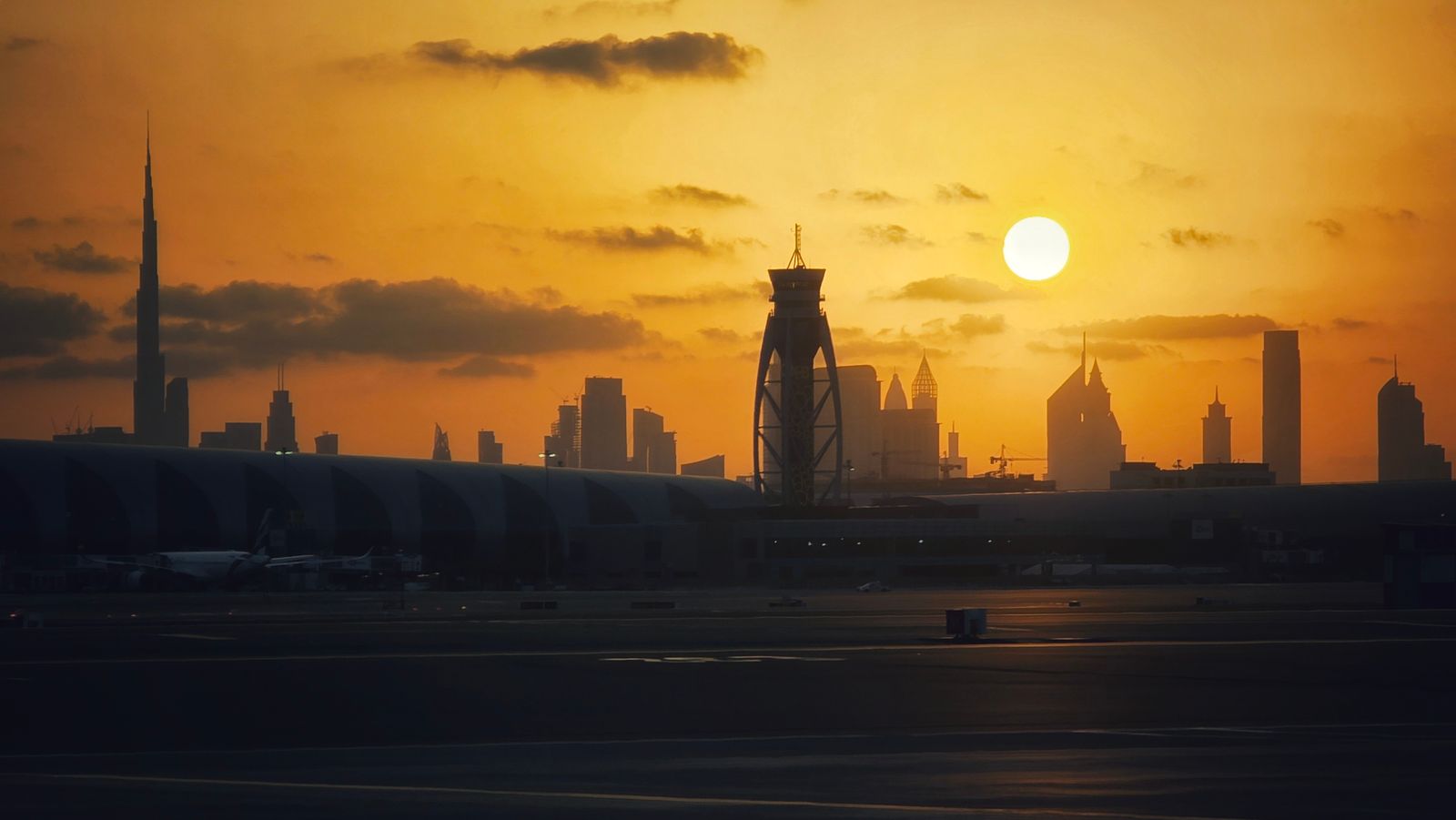 Sunset over Dubai International Airport terminal with the Burj Khalifa and city skyline silhouetted behind