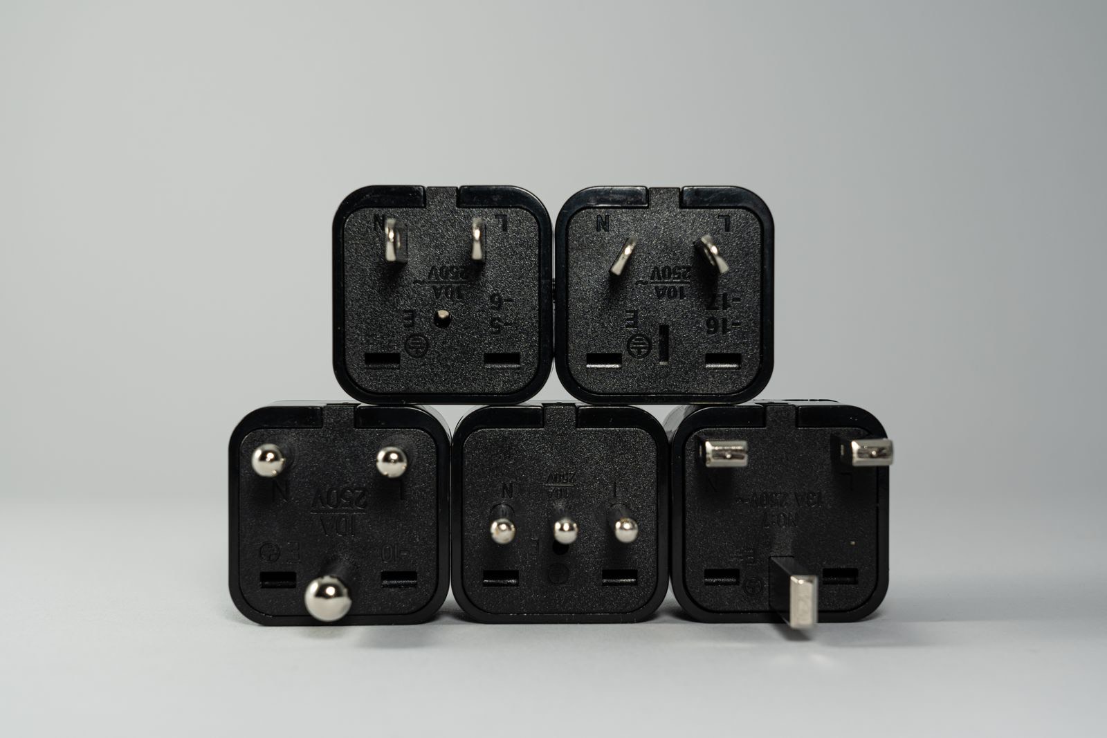 Stack of black travel plug adapters with different pin layouts on a grey background