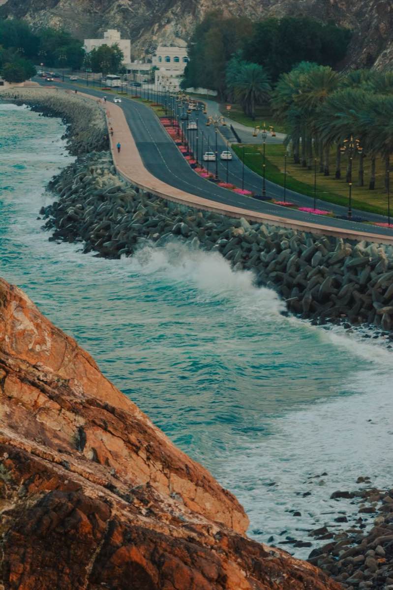 Muscat coastal corniche road beside the sea with palm trees and rocky headland in Oman