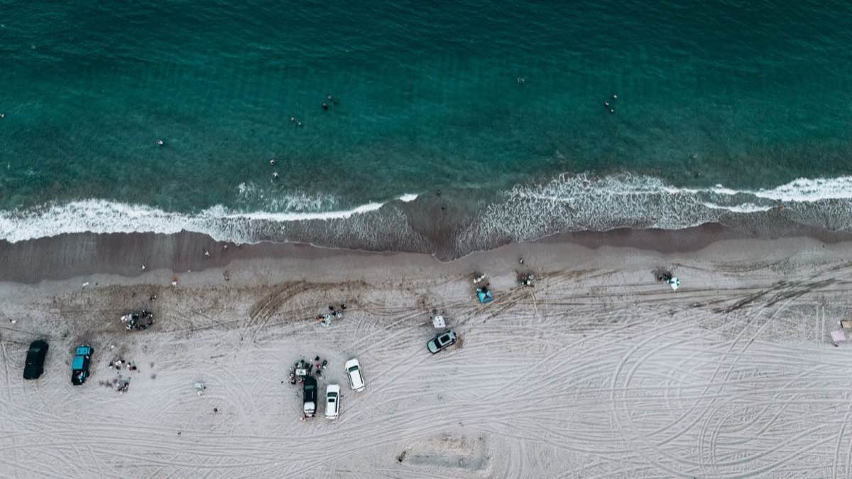 Aerial view of a Fujairah beach on the Gulf of Oman with cars parked on the sand and people in the waves