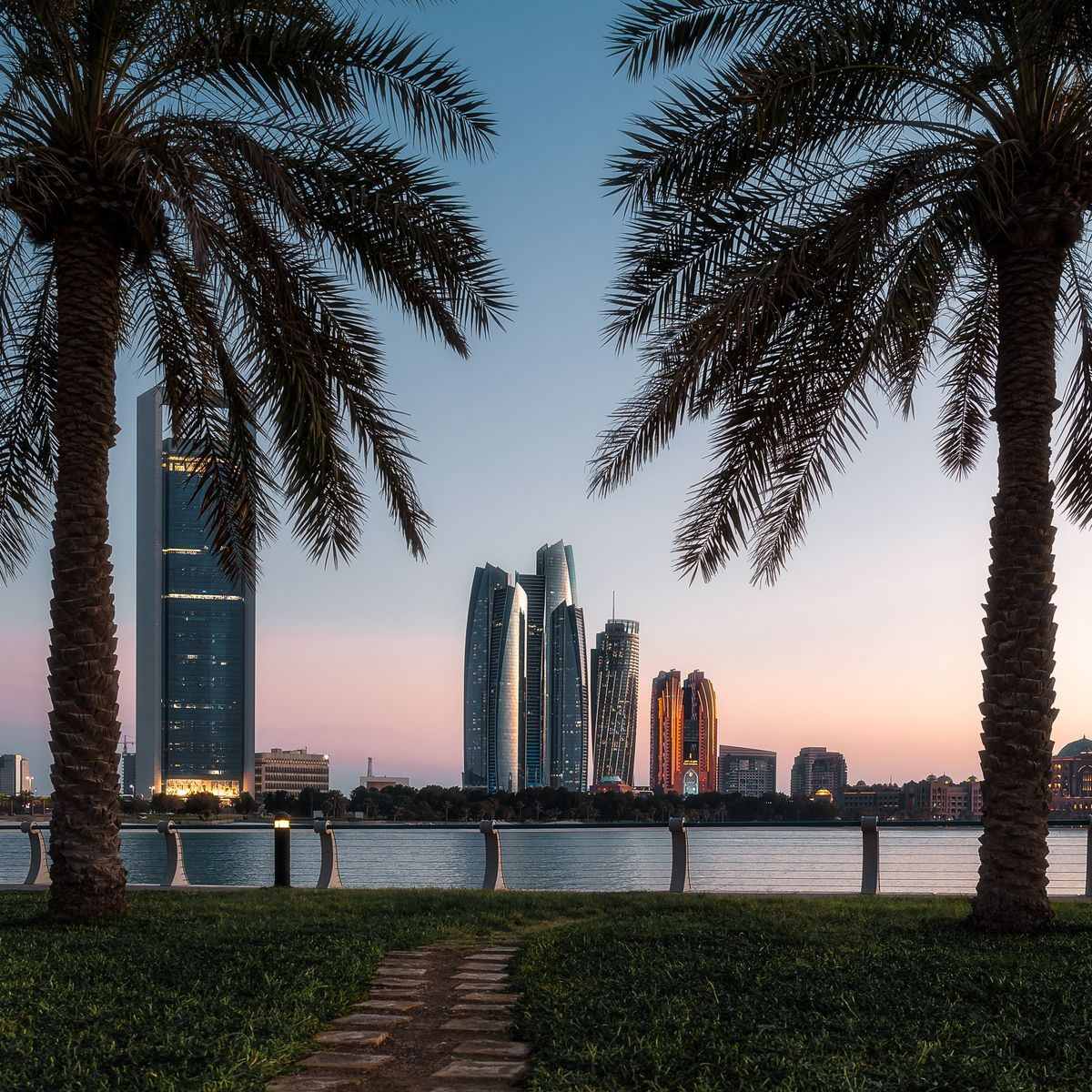 Abu Dhabi towers at dusk framed by date palms