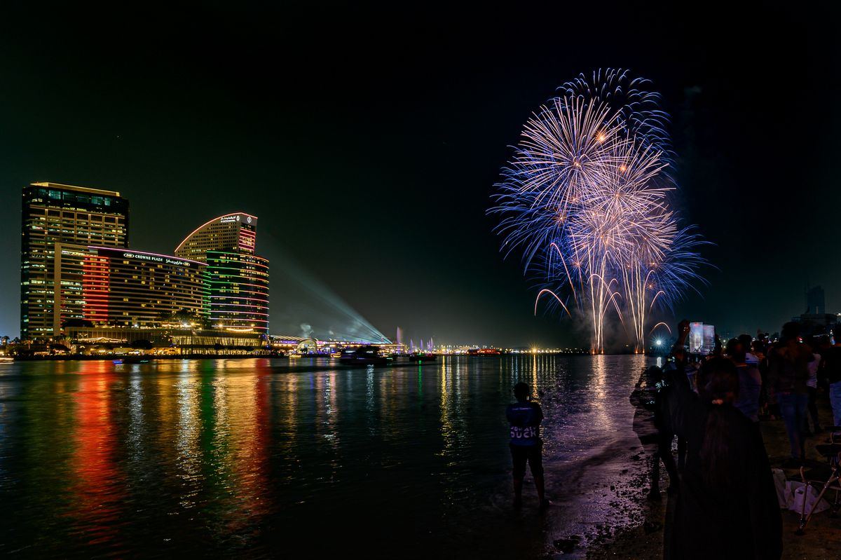 Fireworks over a waterfront hotel with crowd watching at night